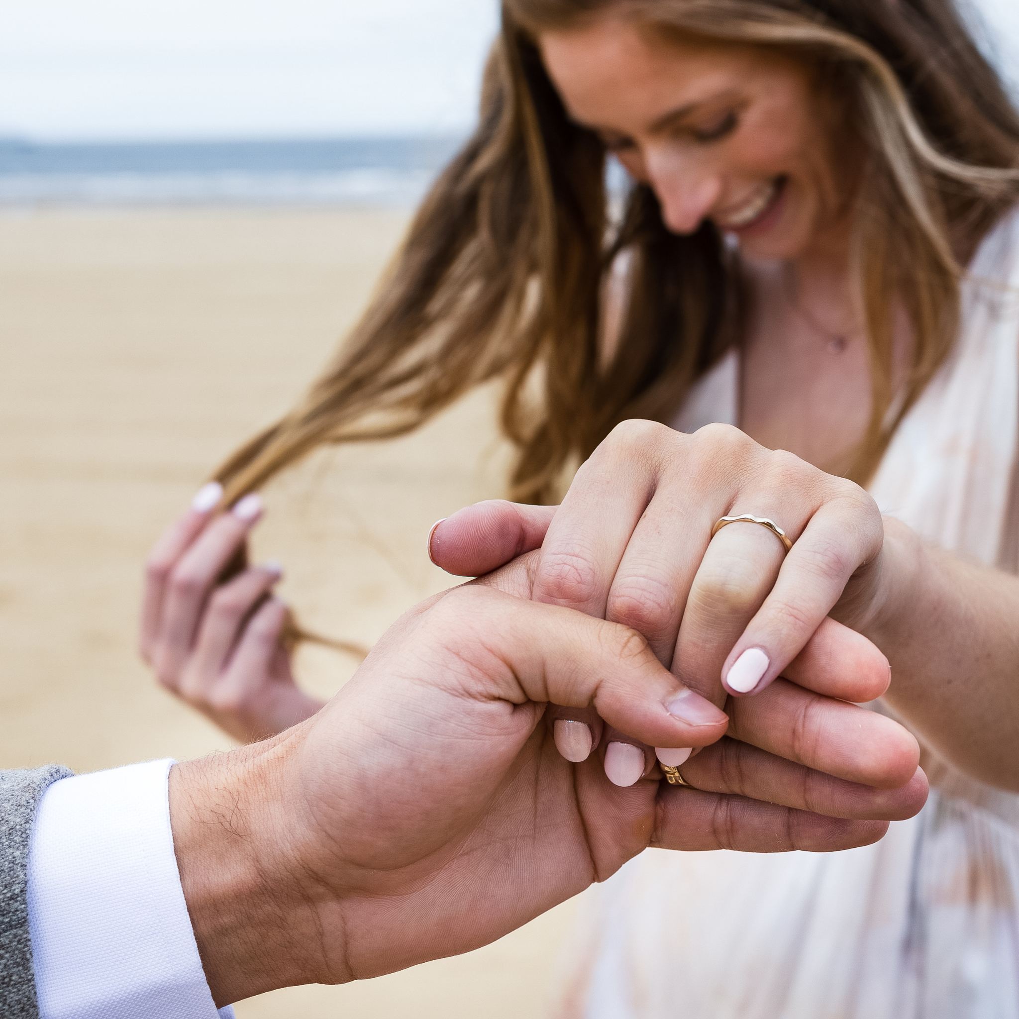 a woman smiling her hand held in a mans hand Ripple Wedding rings 2mm and 5mm recycled yellow gold unique wedding rings unisex male and female by Designer Emma Hedley Claire Collinson Photography