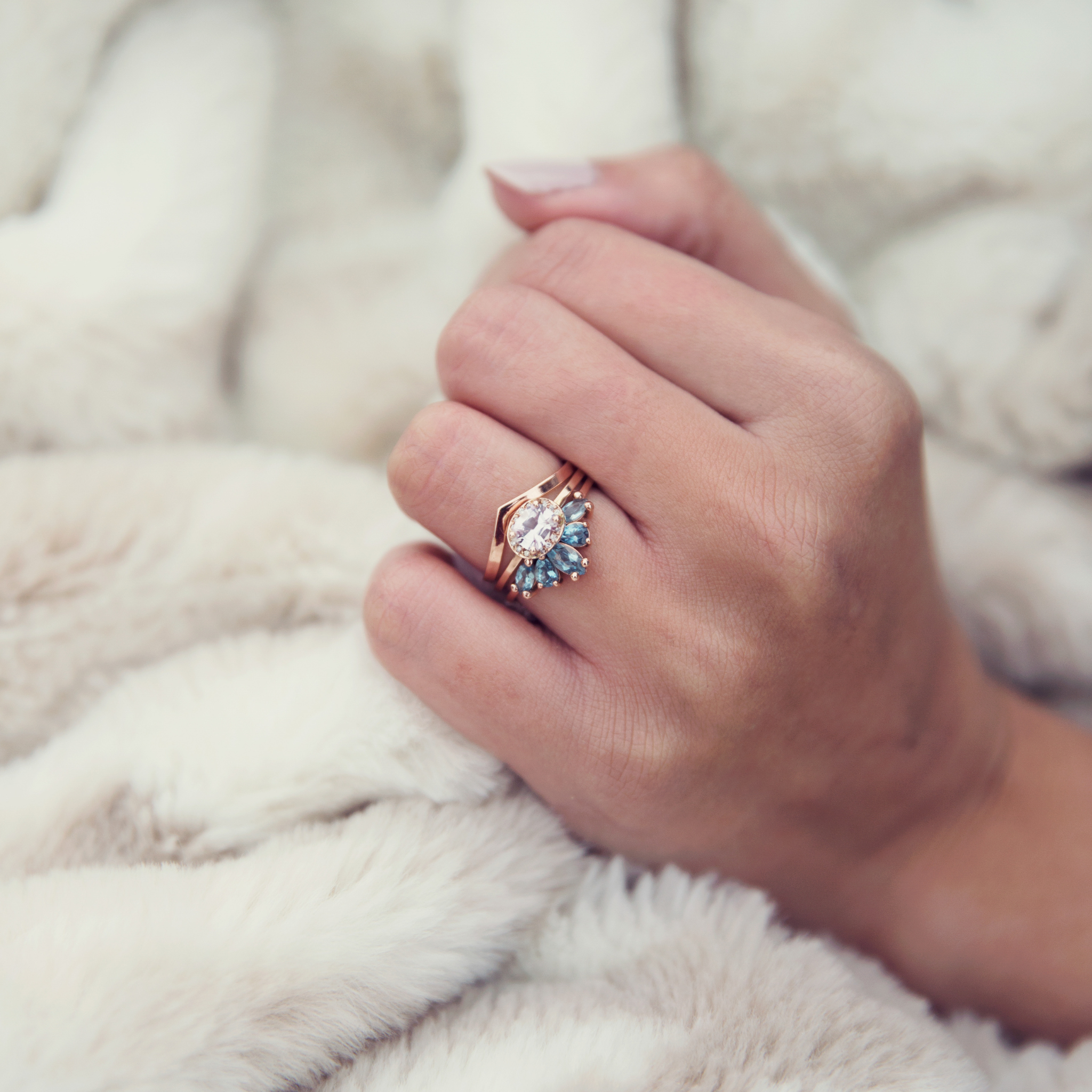 Emma Hedley Fine Jewellery ready to ship gifts wedding engagement eternity ring set stacking rings trio Aqua Radiance Aquamarine rose gold set of 3 stacking rings cushion cut pink sapphire diamond halo wishbone wedding eternity engagement ring set  by Claire Collinson Photography on a female hand with a cozy fur blanket