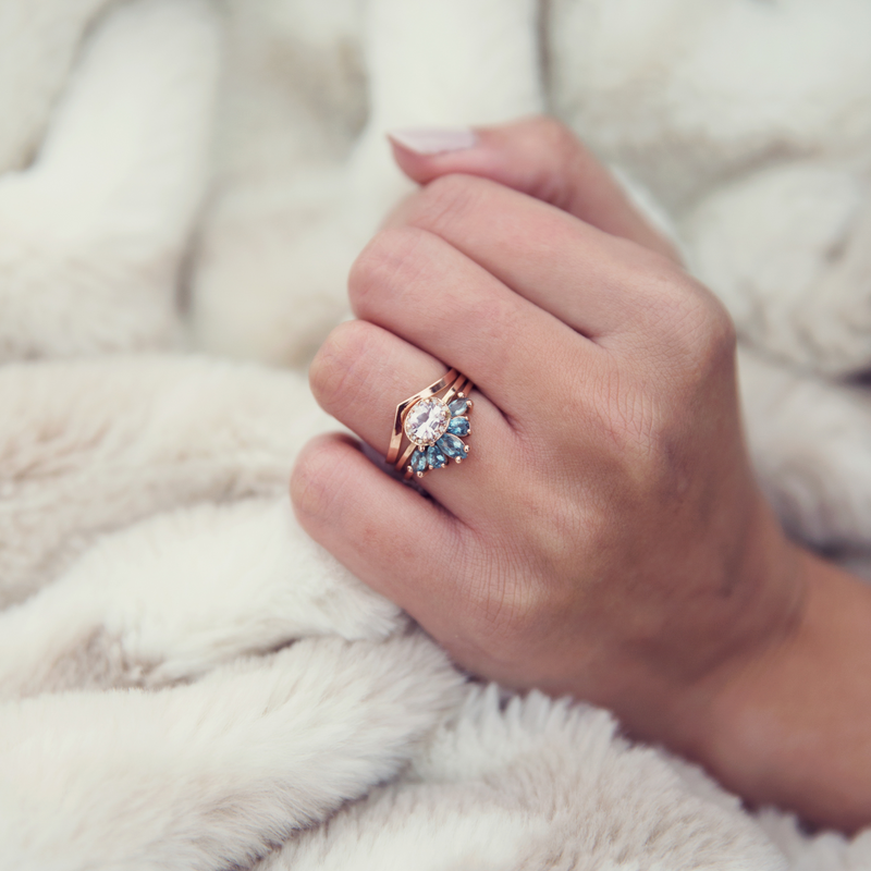 Emma Hedley Fine Jewellery ready to ship gifts wedding engagement eternity ring set stacking rings trio Aqua Radiance Aquamarine rose gold set of 3 stacking rings cushion cut pink sapphire diamond halo wishbone wedding eternity engagement ring set  by Claire Collinson Photography on a female hand with a cozy fur blanket