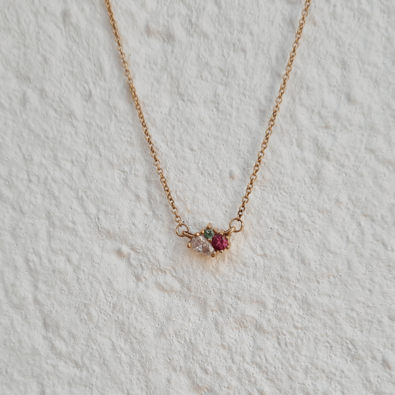 blossom pink and green tourmaline ethically sourced gemstone pendant fine jewellery 18ct recycled rose gold cluster necklace against a white textured wall by designer Emma Hedley