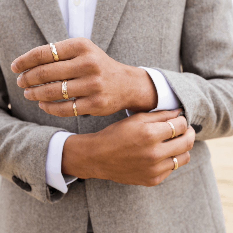 Gold stacking rings worn by a man with a suit modelling Facets 5mm ring Forest and Organic textured cigar wedding rings