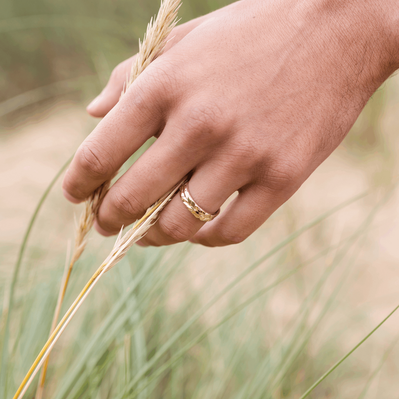 Forest 5mm recycled gold wedding band on a man's hand running through long grass or corn by designer Emma hedley Claire Collinson Photography