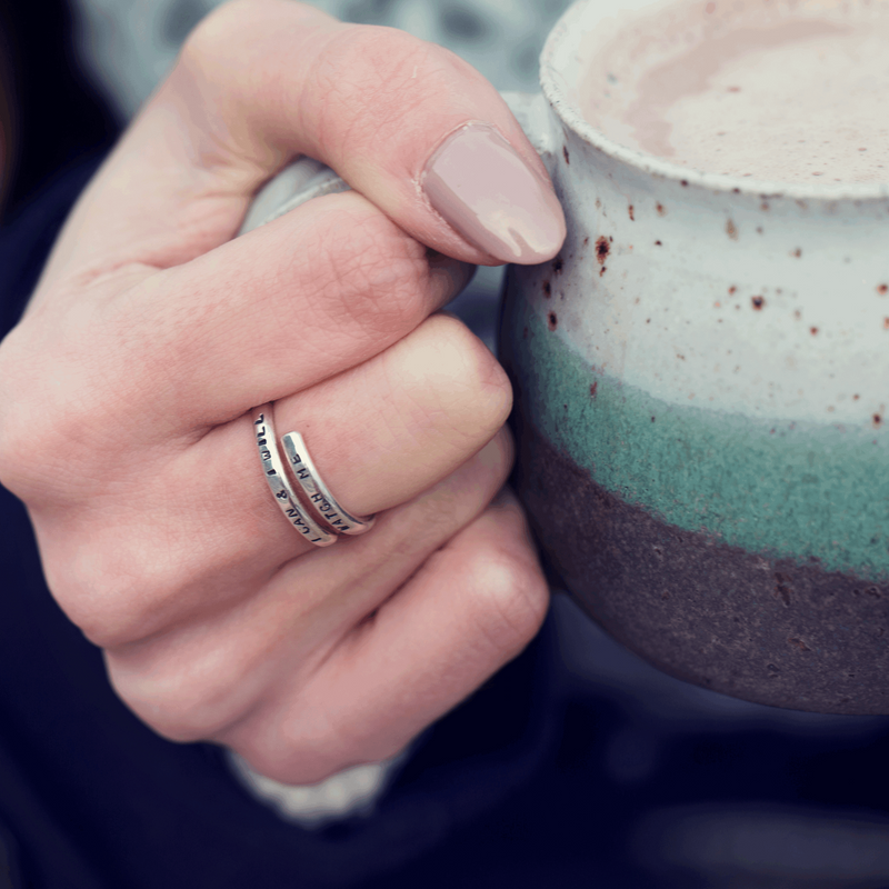 Personalised hand stamped Lyric Adjustable ring worn by a Woman's hand holding a mug. Handmade from Sterling silver by Emma Hedley Artisan Jeweller