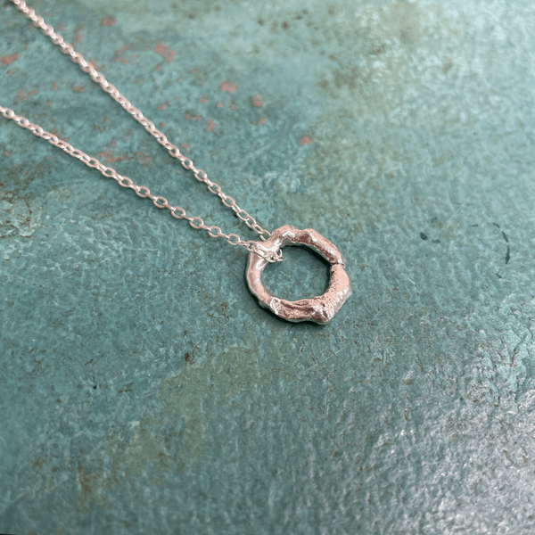 Melted Hoop Pendant using recycled sterling silver hanging on a trace chain in front of a teal background and handmade by Emma Hedley Jewellery 