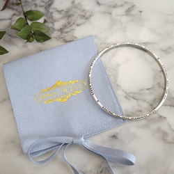 Personalised Lyric bangle with hand stamped custom message handmade from sterling silver, packaged in a recycled ocean plastic baby blue pouch. By Emma Hedley Jewellery Designer
