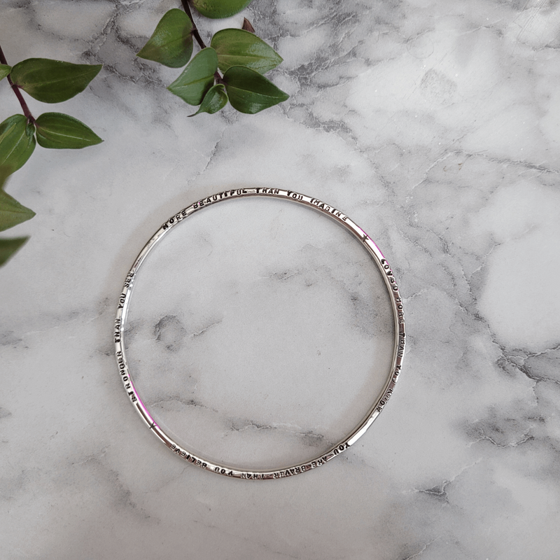 Personalised sterling silver lyric bangle with hand stamped custom message, laid on marble, handmade by Emma Hedley Jewellery